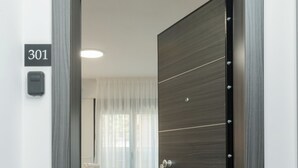 Habitación de hotel moderna con una puerta grande de madera, una cama con sábanas blancas y el número '301' visible en la pared.
