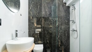 Un baño moderno con un lavamanos blanco, un inodoro y una zona de ducha con mampara de vidrio.