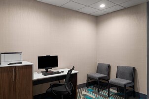 Una habitación de hotel con escritorio, computadora, impresora, dos sillas y un tapete estampado.