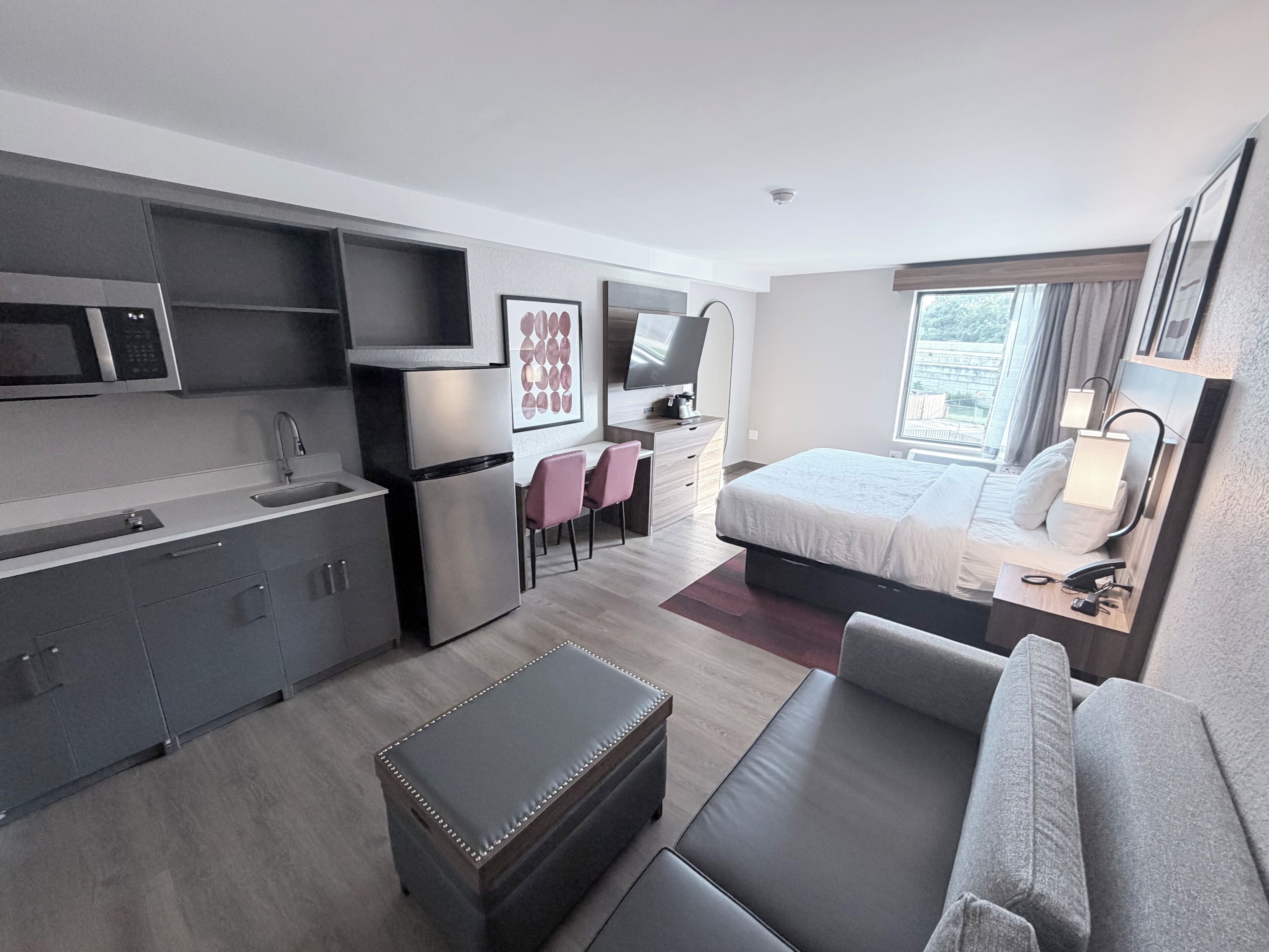 Una habitación de hotel moderna con kitchenette, una cama, un sofá y un escritorio con una silla.
