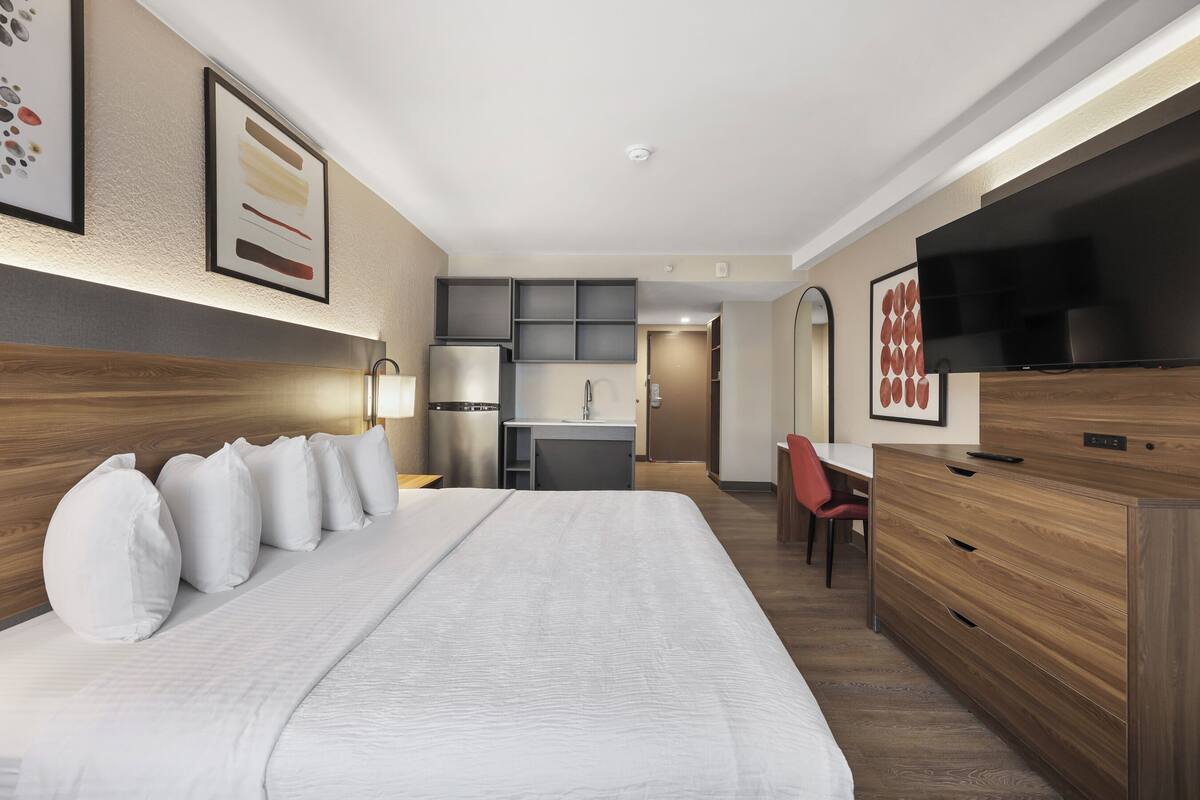 Quarto de hotel com uma cama grande, uma escrivaninha, uma televisão e uma kitchenette.