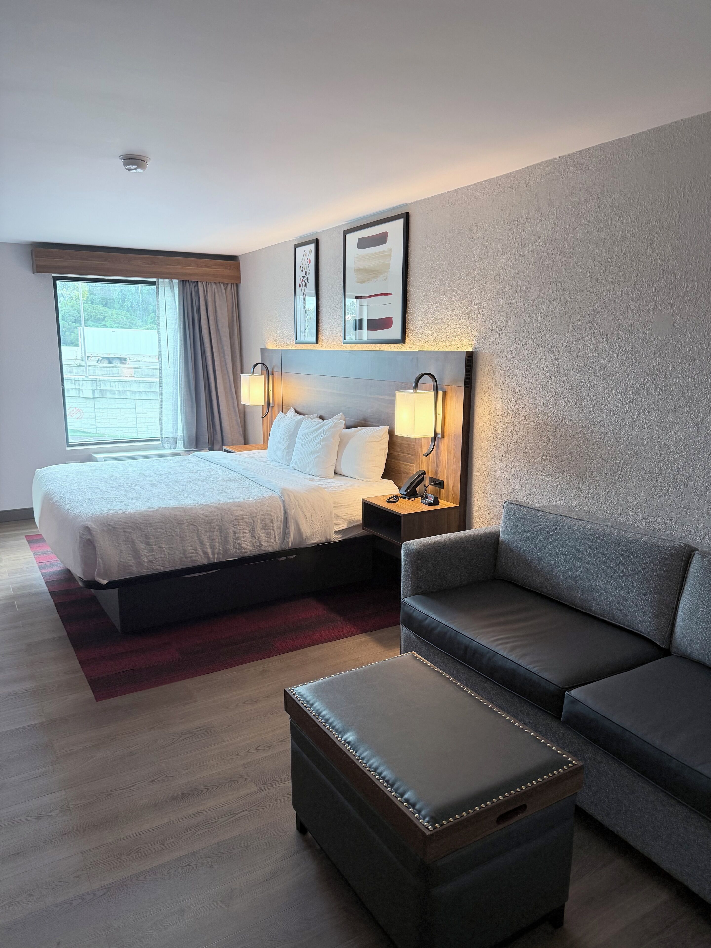 Une chambre d’hôtel avec un lit, des lampes de chevet, un canapé, une table basse et une fenêtre avec des rideaux.