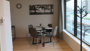 Een moderne eetruimte met een ronde tafel, zes stoelen, een klok en een schilderij van bomen aan de muur.
