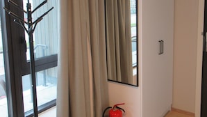Een kamer met een raam, een brandblusser, een kapstok en een kledingkast.