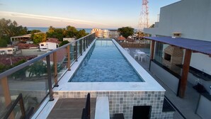Piscina infinita no terraço, com guarda-corpo de vidro, com vista para a cidade e o mar.