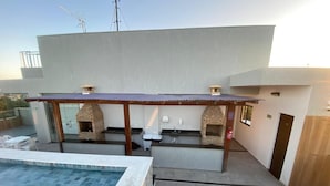 Um terraço no telhado com piscina, cozinha ao ar livre e dois fornos de tijolo.