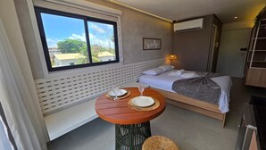 Um quarto com uma cama, uma mesa com pratos e copos, uma janela com vista e um ar condicionado fixado na parede.