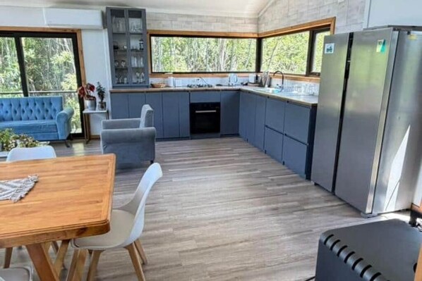 A modern kitchen with grey cabinets, a stainless steel refrigerator, and a dining area with a wooden table and chairs.