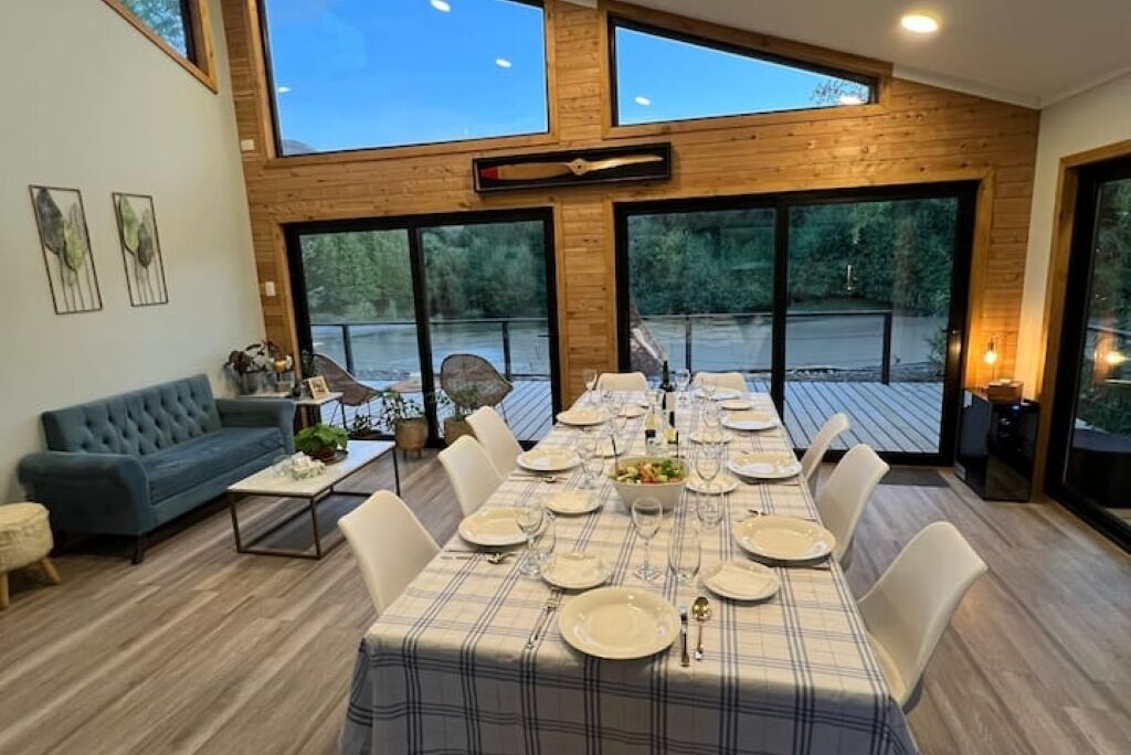 Un espace repas avec une longue table dressée pour le repas, de grandes fenêtres et une vue sur l’extérieur.