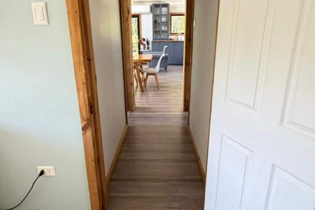 A narrow hallway with wooden flooring leading to a kitchen area.