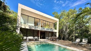 Et moderne hus med swimmingpool, omgivet af frodig vegetation.