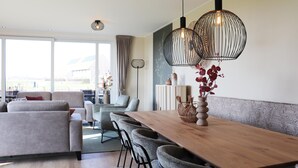 A modern living room with a wooden dining table, grey sofas, and a patterned wall. - Luxury Waterfront Villa (Leons)