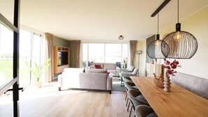 A spacious living area with a wooden dining table, sofas, and a large window. - Luxury Waterfront Villa (Leons)
