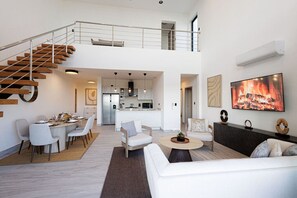 A spacious living area with a staircase, a dining set, a kitchen, and a large flat-screen TV.