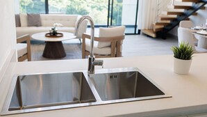 Une cuisine moderne dotée d’un évier en acier inoxydable, d’un plan de travail blanc et offrant une vue sur un espace de vie comprenant un canapé et une table basse.