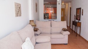A living room with a beige sofa, a lamp, and a kitchen in the background. - 3 Bedroom Ground FloorApartment (MOJACAR)