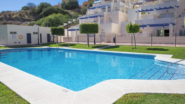 A swimming pool with a clear blue water, surrounded by a paved area and a building with multiple balconies. - 3 Bedroom Ground FloorApartment (MOJACAR)