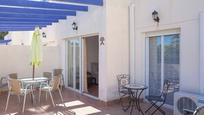 An outdoor patio with a table and chairs, a covered area with blue beams, and an air conditioning unit. - 3 Bedroom Ground FloorApartment (MOJACAR)
