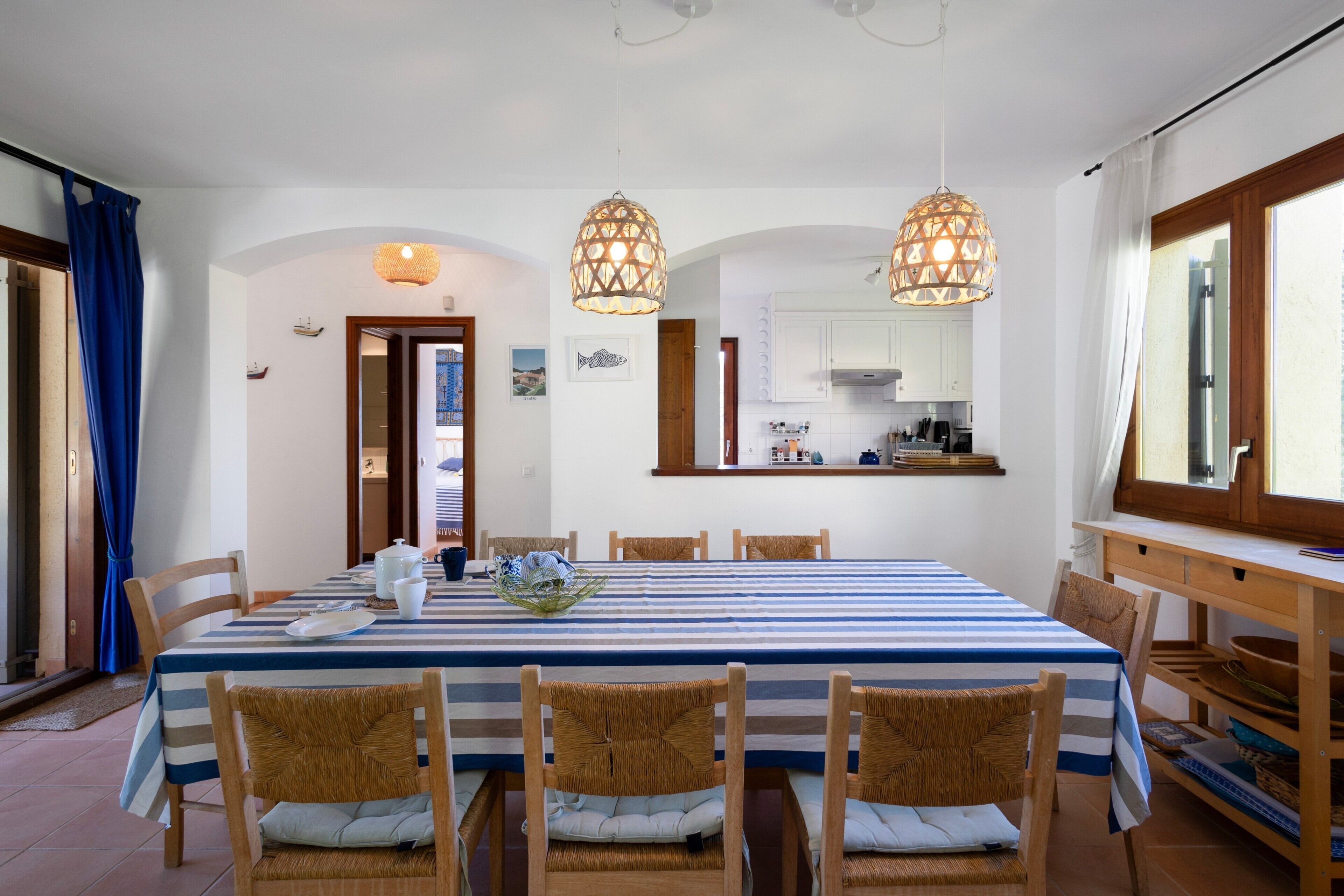 Un comedor con mantel a rayas, sillas de mimbre y lámparas colgantes.