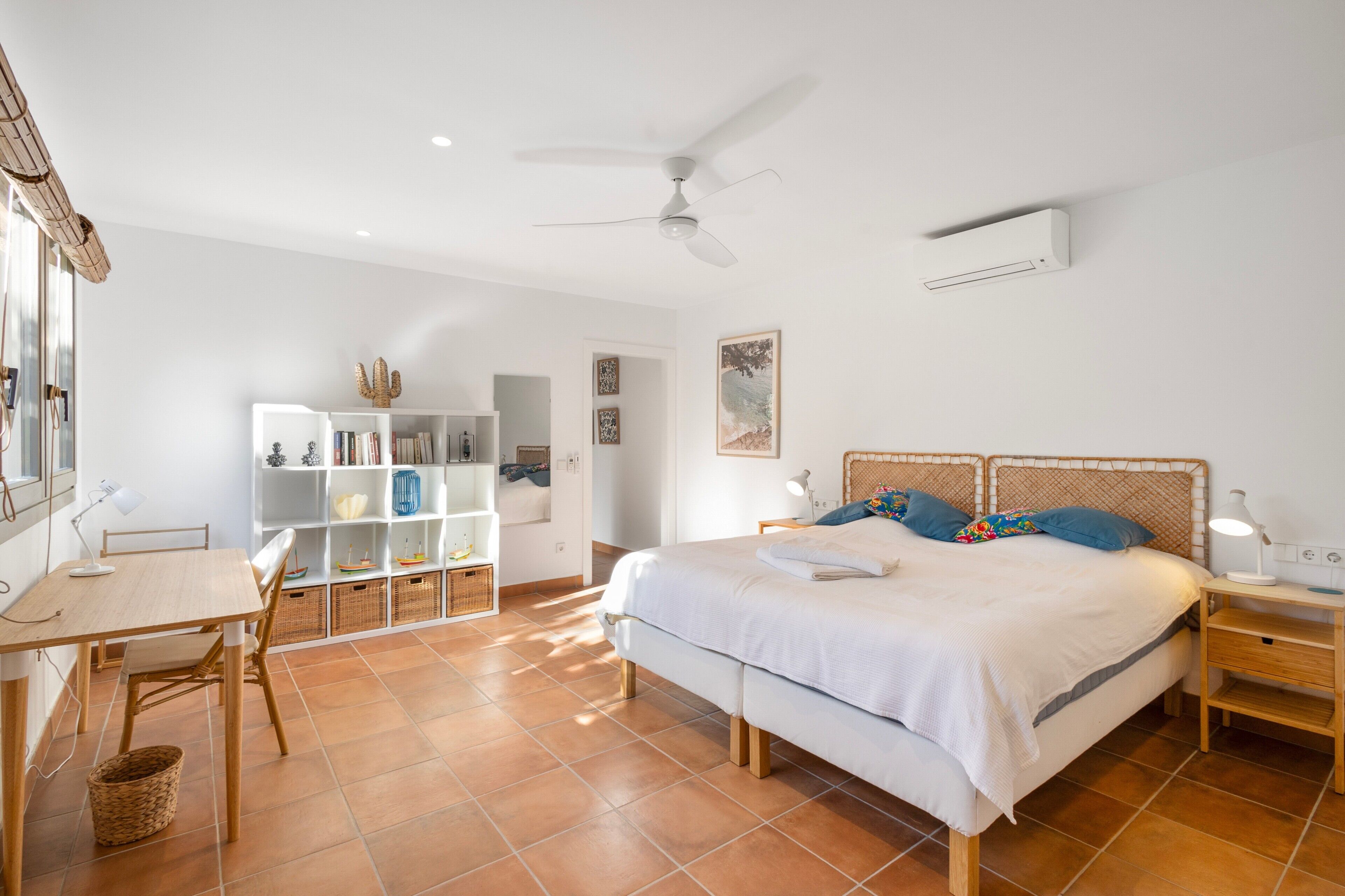 Un dormitorio con cama, escritorio, estantería, ventilador de techo y aire acondicionado.