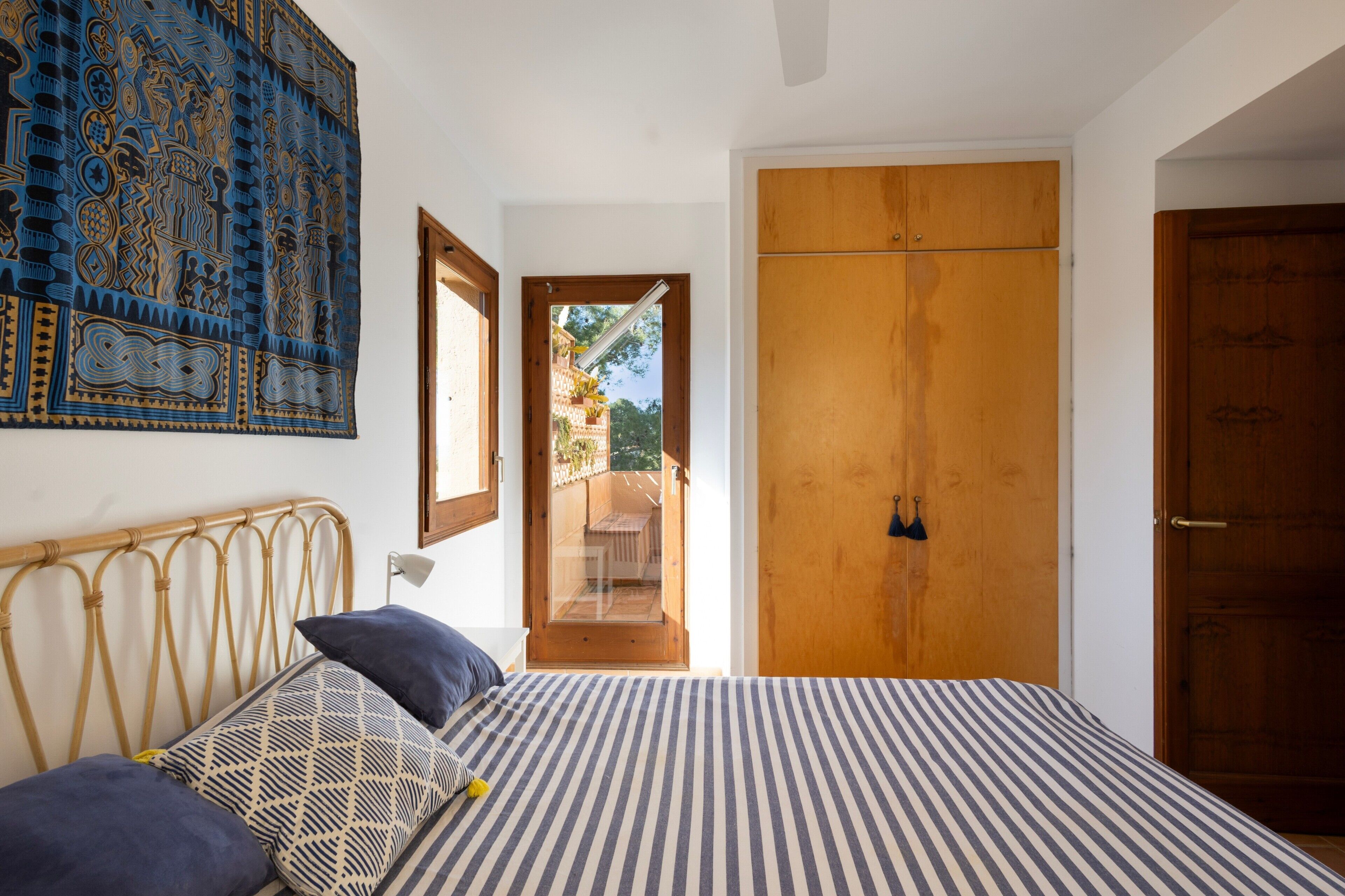A bedroom with a bed, a wooden wardrobe, a door, and a view through an open door.