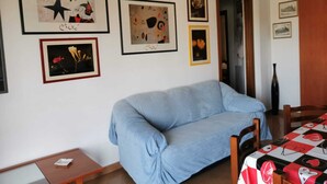 Olohuoneessa on sininen sohva, pieni pöytä ja seinällä on useita erilaisia kehystettyjä taideteoksia.