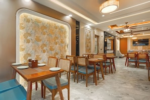 Un restaurante con mesas y sillas de madera, un muro con diseño y un techo con iluminación empotrada.
