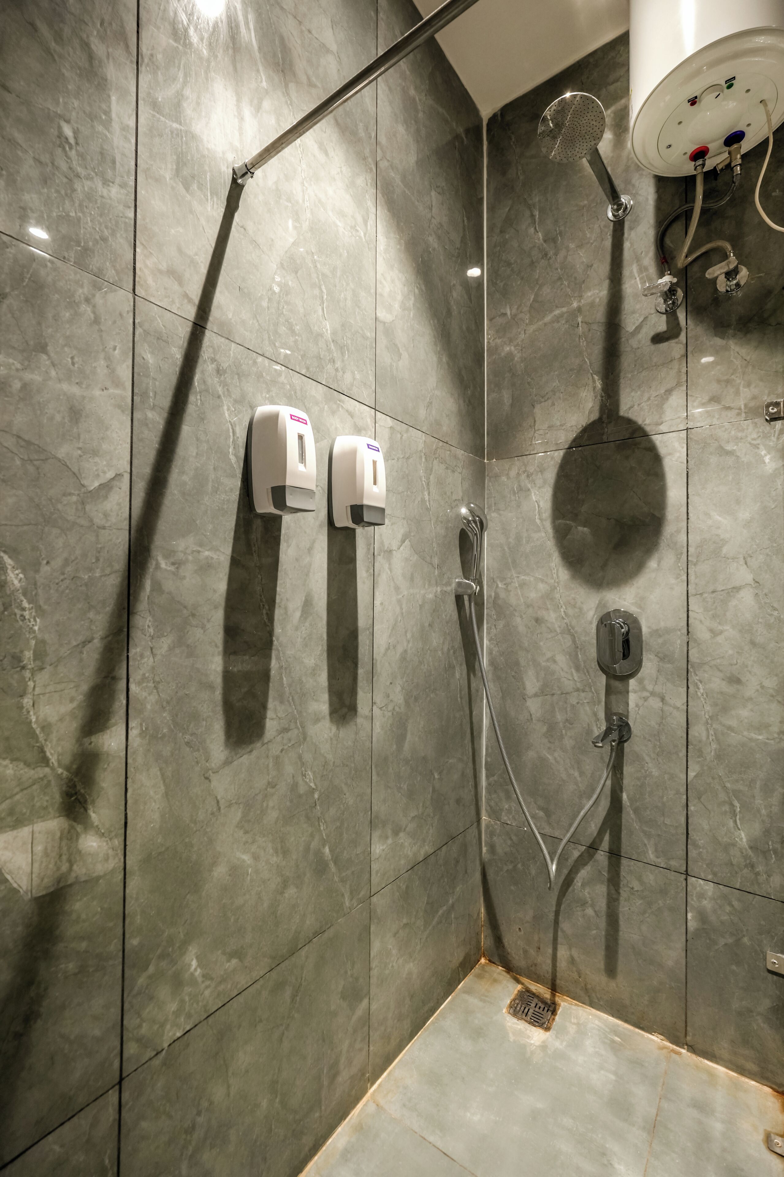 Área de duche com chuveiro manual, secador de mãos fixado na parede e ralo no chão.