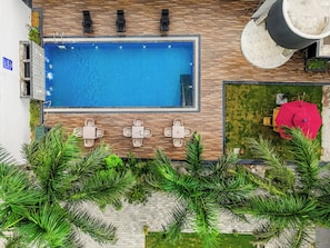 An aerial view of a swimming pool with lounge chairs, a table, and surrounding greenery.