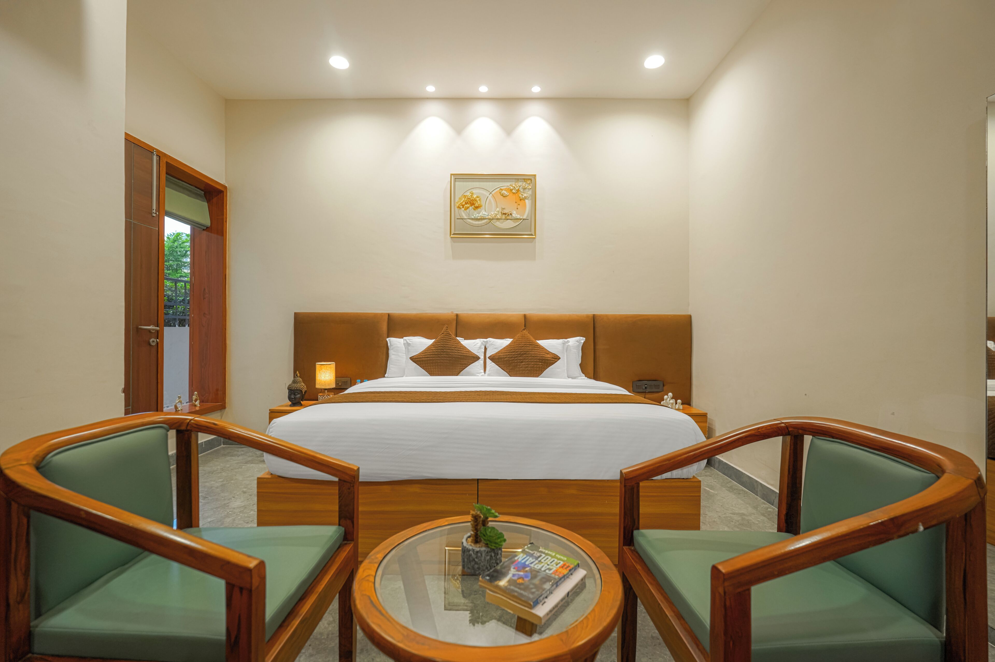 Une chambre d’hôtel avec un grand lit, deux fauteuils, une petite table et un tableau au mur.