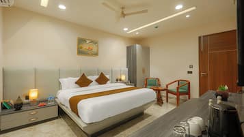 A hotel room with a bed, bedside tables, a desk, a chair, a ceiling fan, and a painting on the wall.