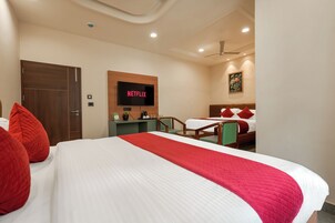 Una habitación de hotel con una cama, un escritorio, un televisor mostrando 'NETFLIX' y un cuadro en la pared, además de una puerta.