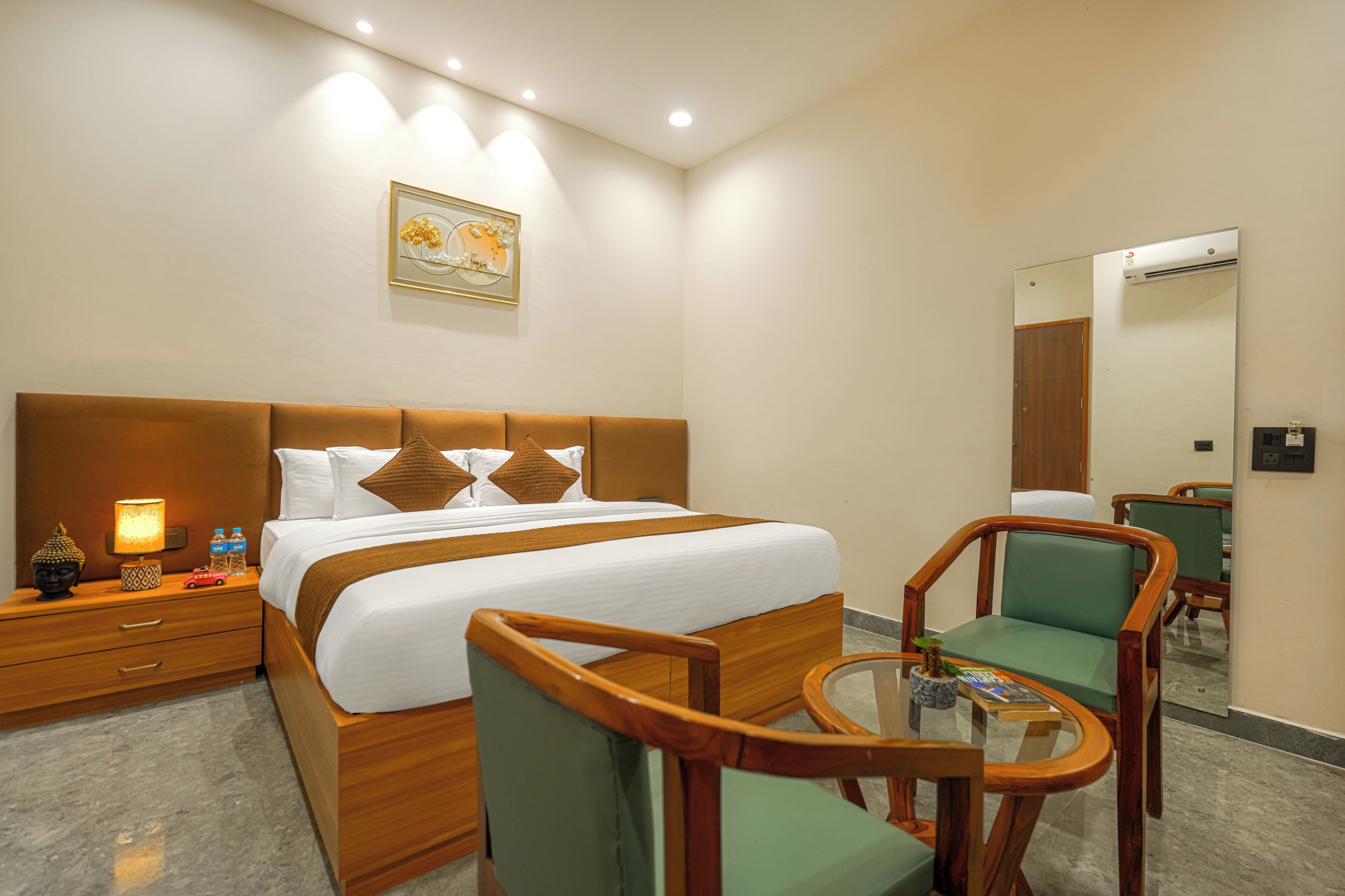 Habitación de hotel con cama, mesita de noche, lámpara, dos sillas, una pequeña mesa y un espejo.