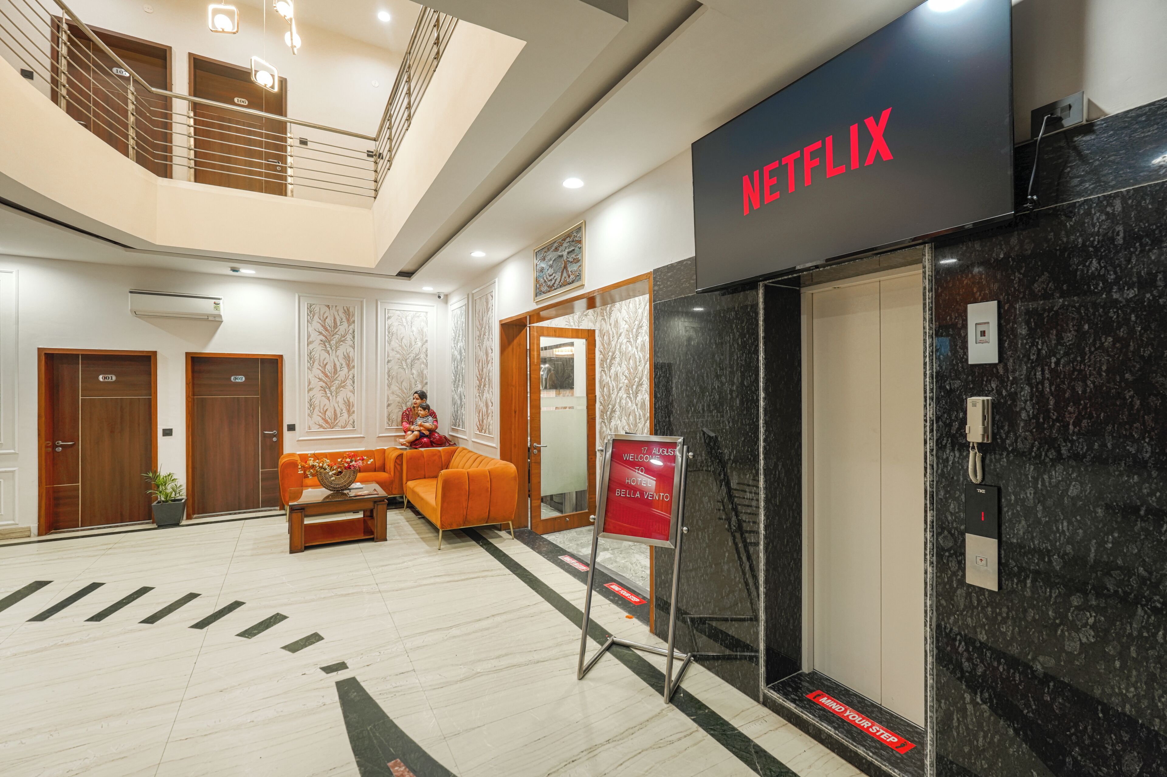 A hotel lobby with a Netflix sign, a reception desk, a staircase, and a seating area.