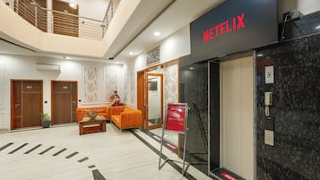 A hotel lobby with a Netflix sign, a reception desk, a staircase, and a seating area.