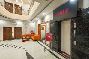 Et hotel lobby med et Netflix skilt, en receptionsdisk, en trappe og et siddeområde.