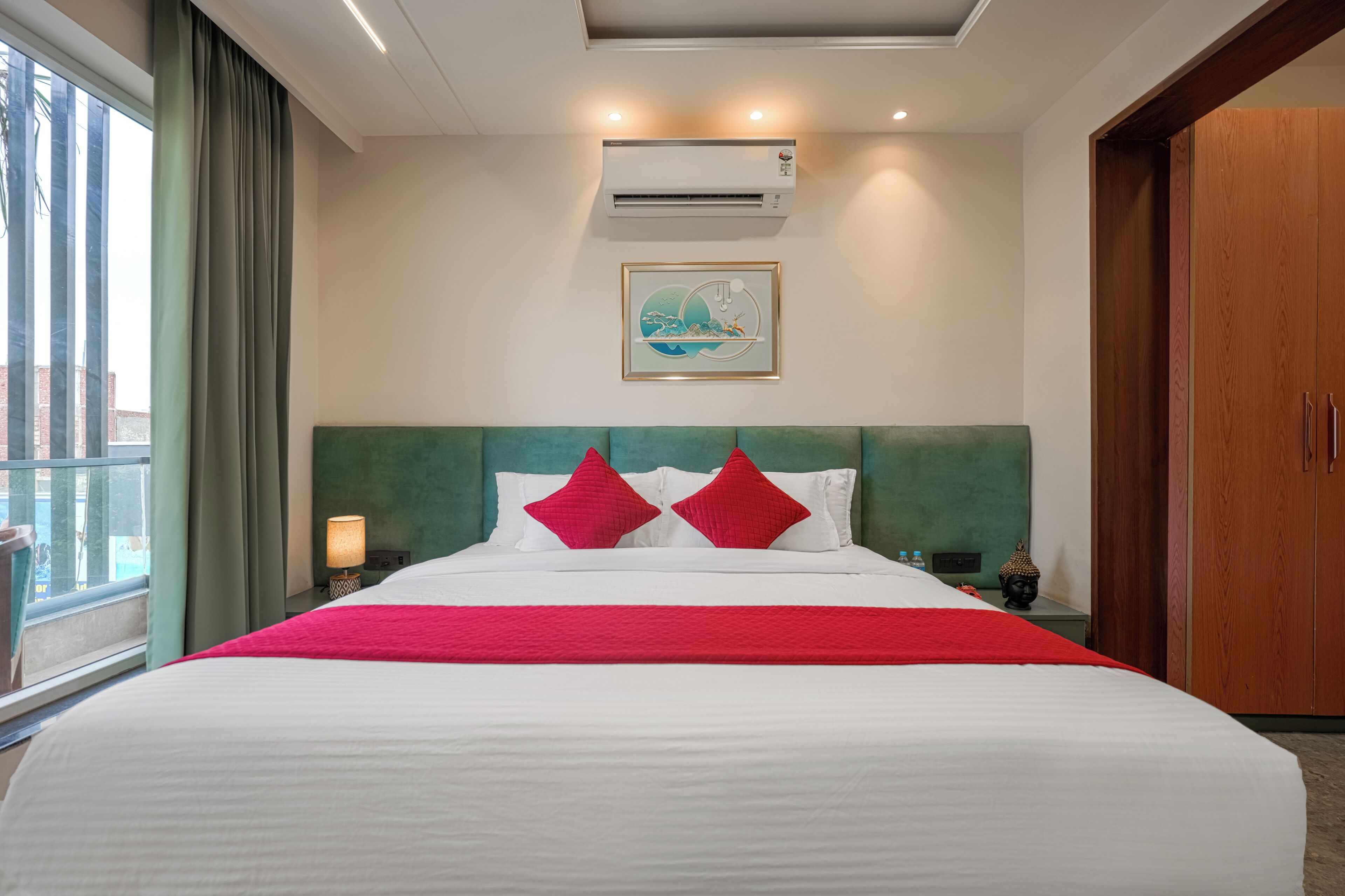Quarto de hotel com uma cama grande, cabeceira, ar condicionado, um quadro na parede e uma janela com cortinas.