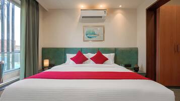 Quarto de hotel com uma cama grande, cabeceira, ar condicionado, um quadro na parede e uma janela com cortinas.