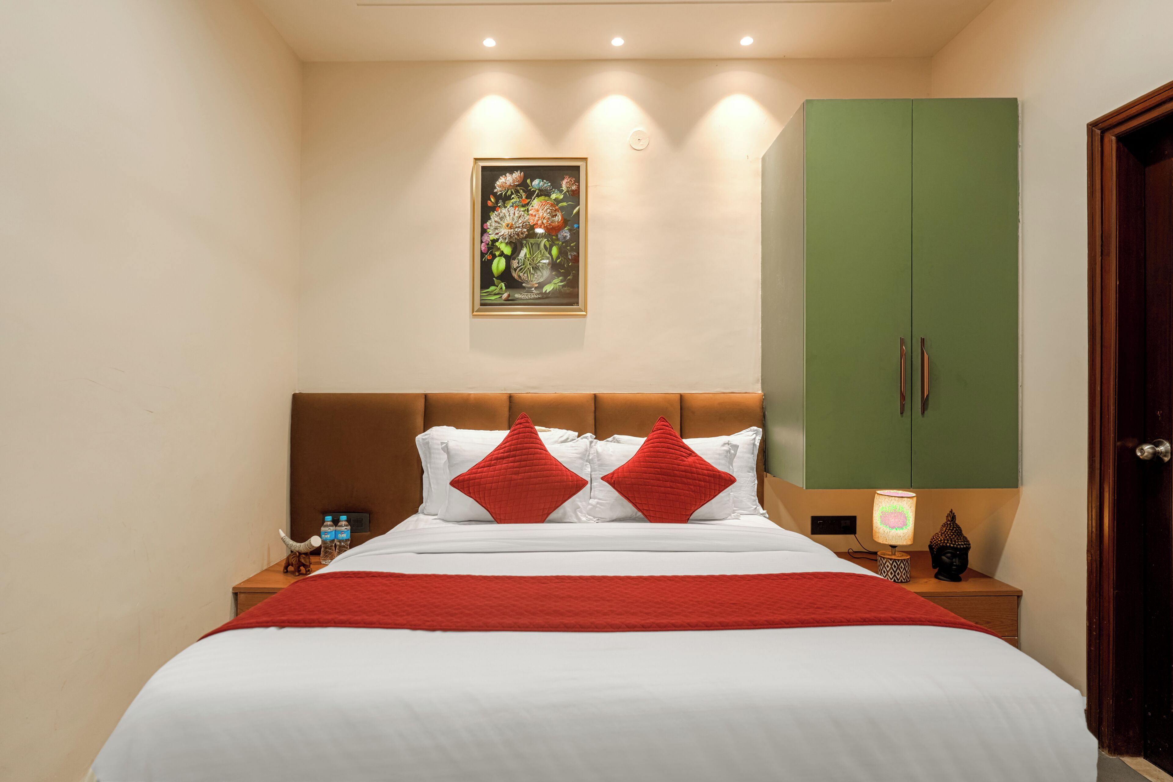 Una habitación de hotel con una cama, un armario verde, una mesita de noche con una lámpara y un cuadro colgado en la pared.