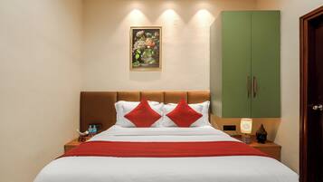 Una habitación de hotel con una cama, un armario verde, una mesita de noche con una lámpara y un cuadro colgado en la pared.
