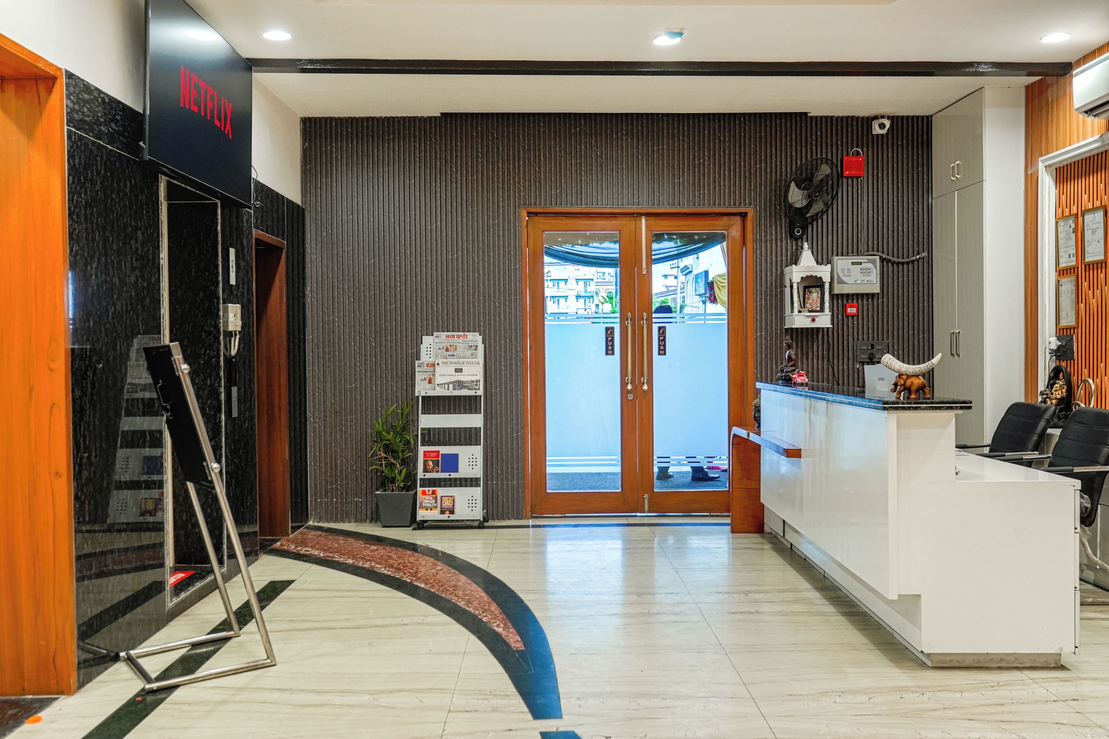 A reception area with a modern design, including a reception desk, a wall-mounted fan, and a potted plant.