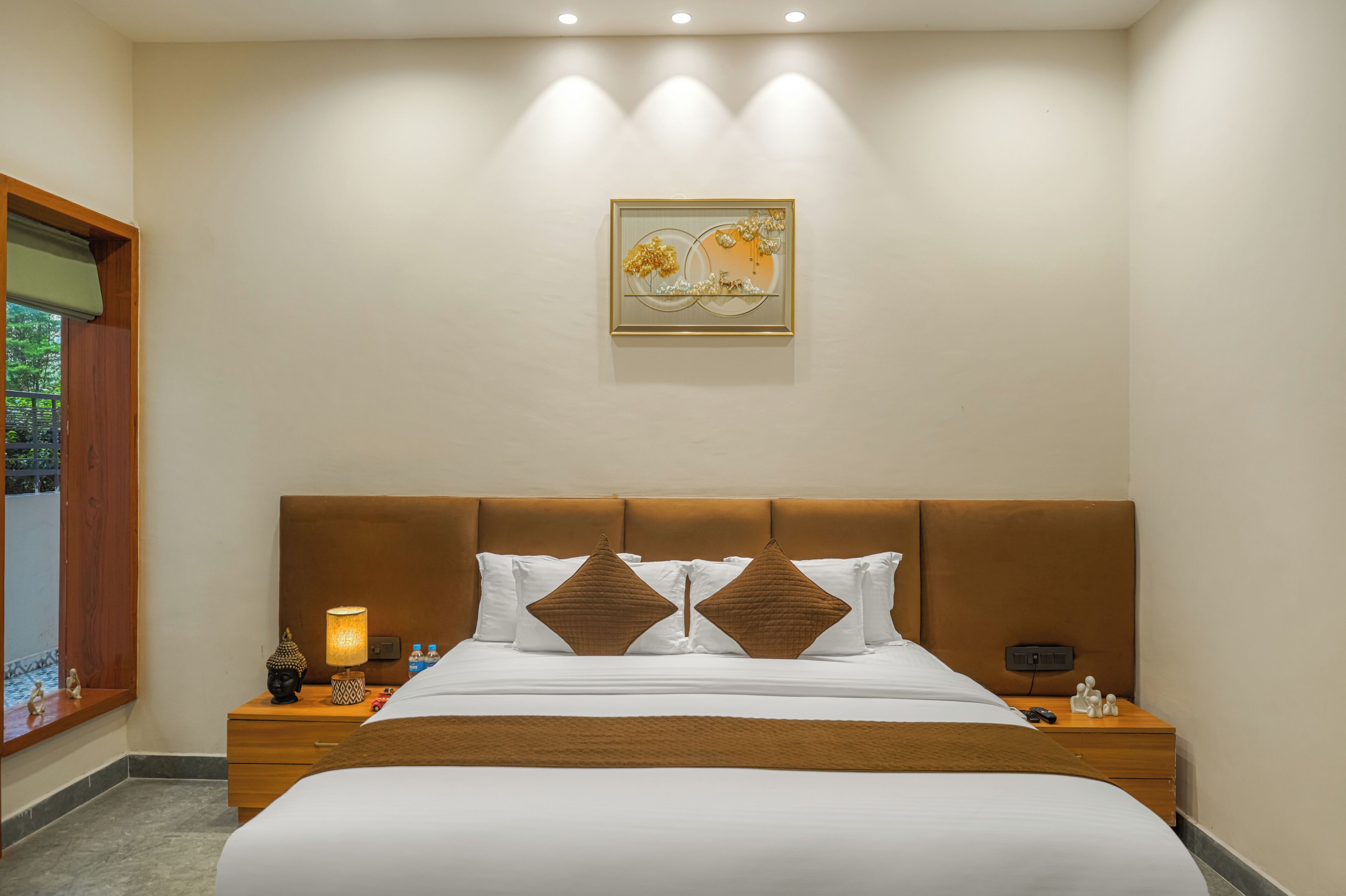 A hotel room with a large bed, two bedside tables, a nightstand, a wall-mounted artwork, and a window with a view.