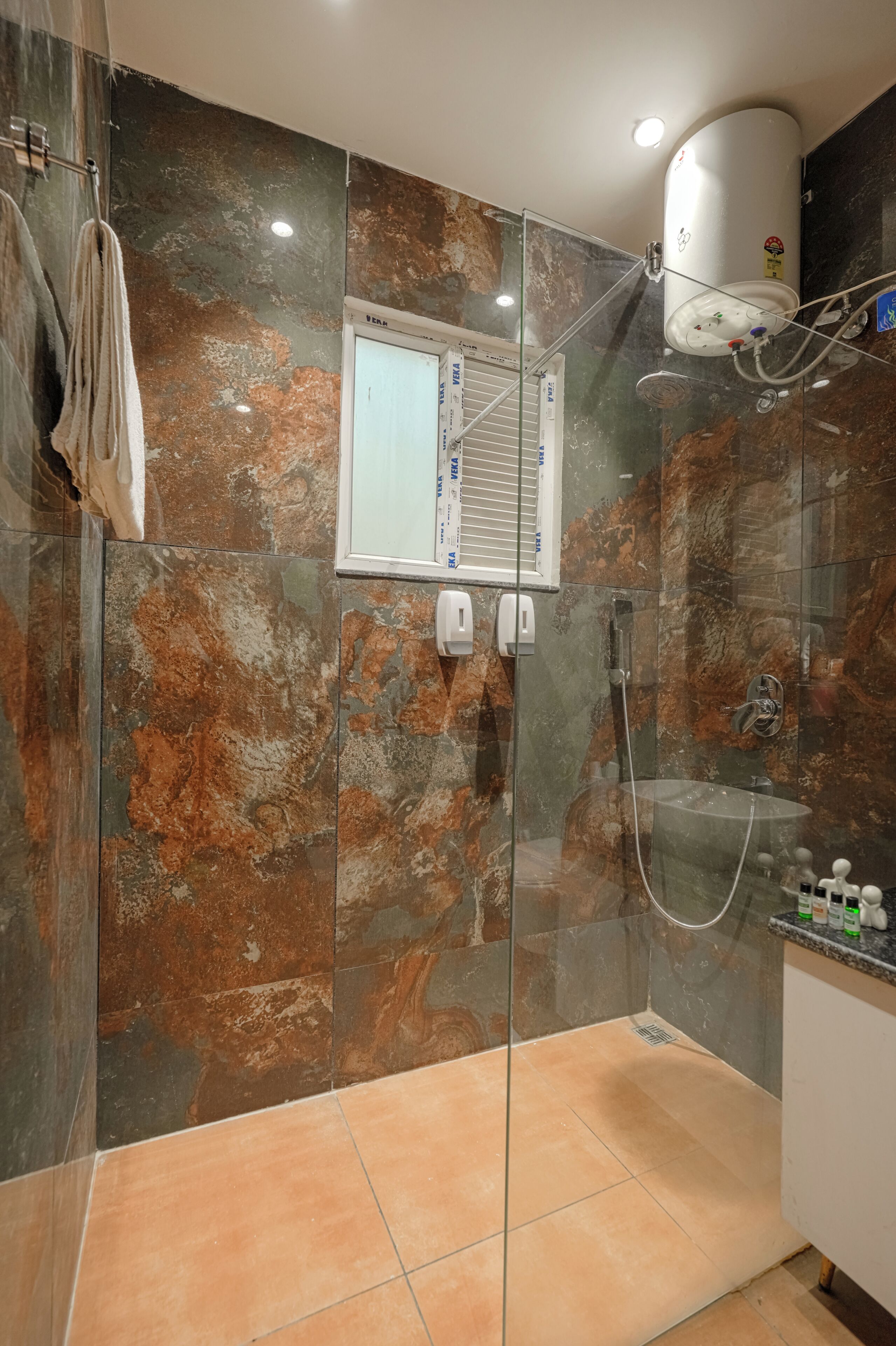 Ducha con cerramiento de vidrio, un ventanal integrado, perchero y calentador de agua en la pared.