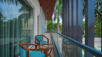 A balcony with a glass balustrade, two wooden chairs, and a small table with a cup.