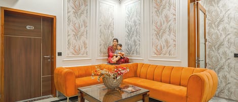 Una habitación con puerta de madera, un sofá, una mesa de centro de vidrio y una pared cubierta de papel tapiz floral.