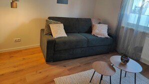 Ein modernes Wohnzimmer mit einem dunkelgrünen Sofa, zwei Beistelltischen, einem Couchtisch und einem Gemälde an der Wand.