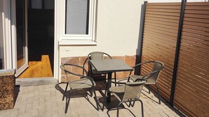 Eine Terrasse mit Tisch und Stühlen, einer Schiebetür und einer weißen Wand.