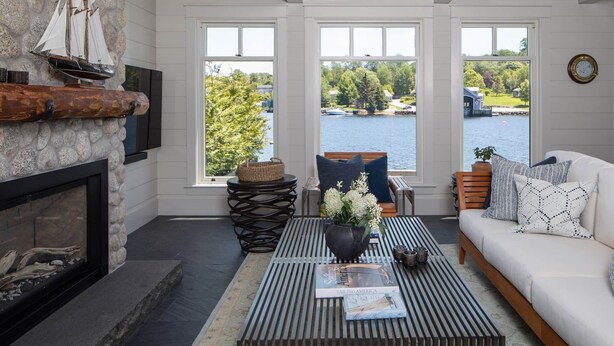 A cozy living room with a fireplace, a coffee table with books, a sofa, and a view of a lake. - Chester Back Harbour Exclusive providing direct access to water via private dock (Chester Basin)