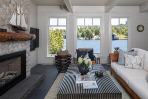 Una sala de estar acogedora con chimenea, una mesa de centro con libros, un sofá y vistas a un lago.