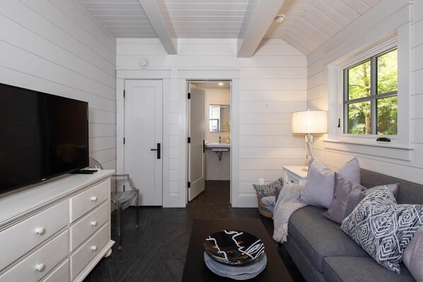 Una habitación con televisor, un sofá con cojines estampados, una ventana con vistas y una puerta que da a un baño.